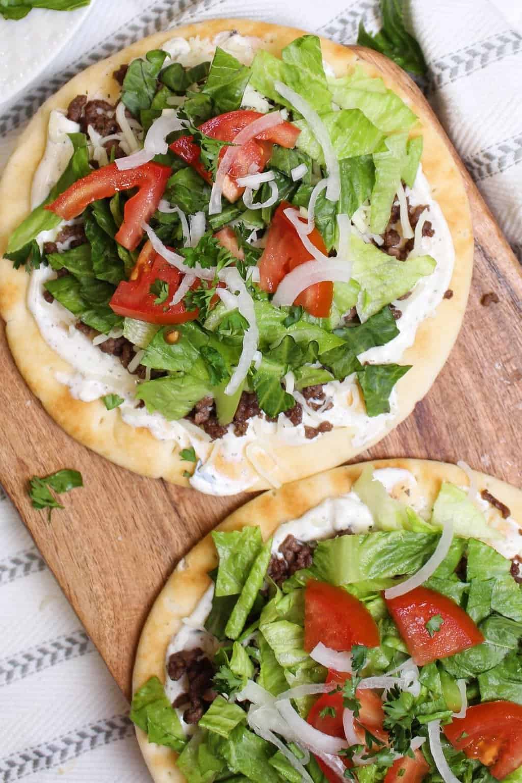Two Greek pizzas on a cutting board.