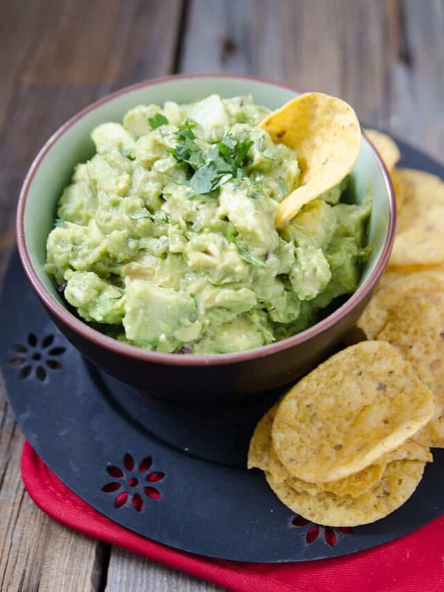 Homemade guacamole on a bowl with some tacos beside it.