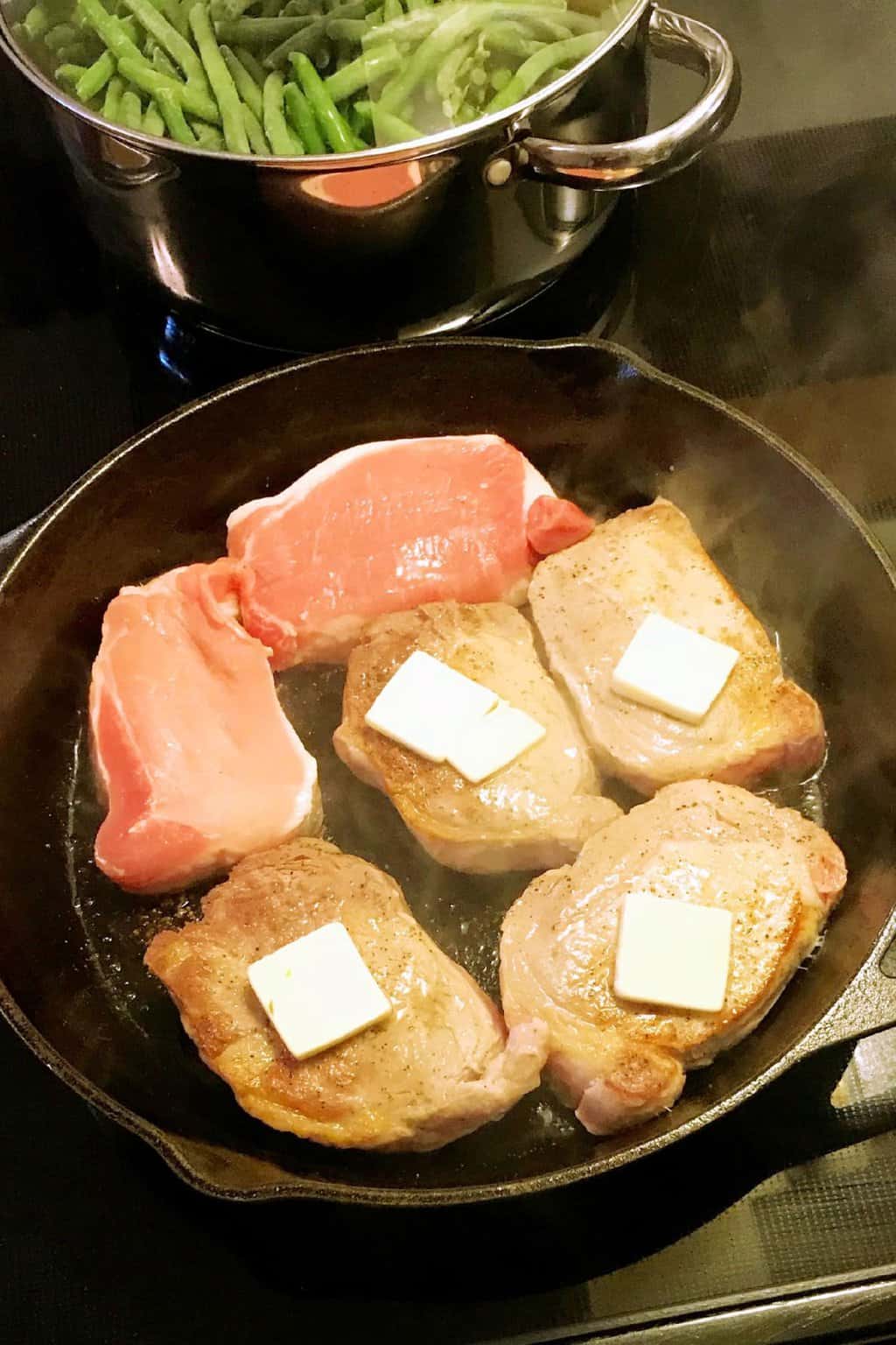 Pork chops cooking on a skillet with butter on top.