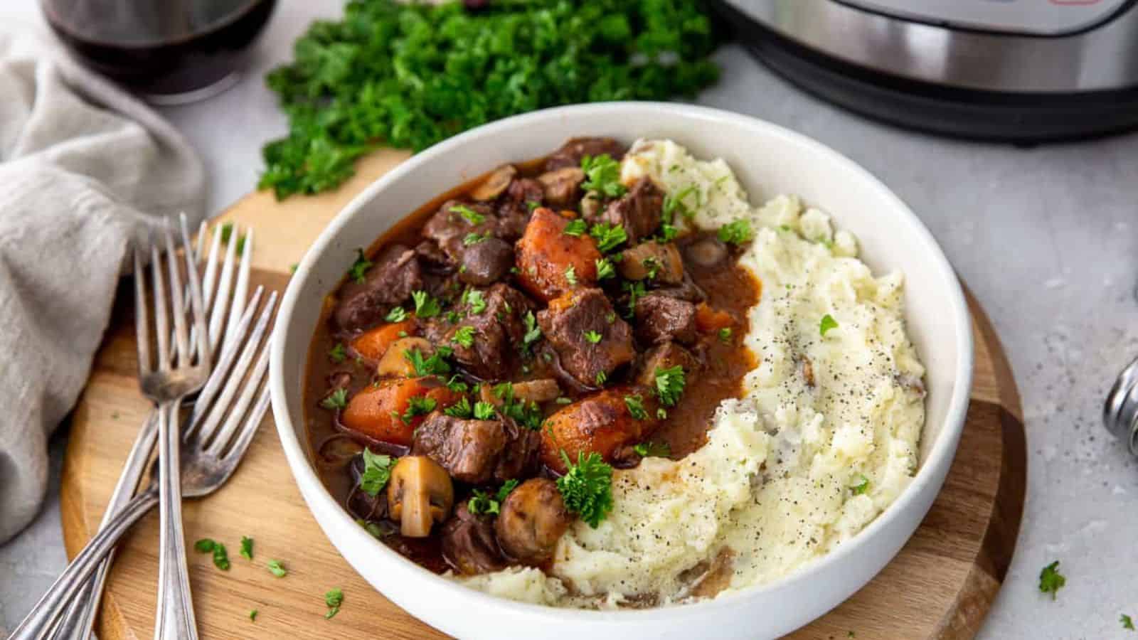 A bowl of mashed potatoes with beef, veggies and burgundy sauce.