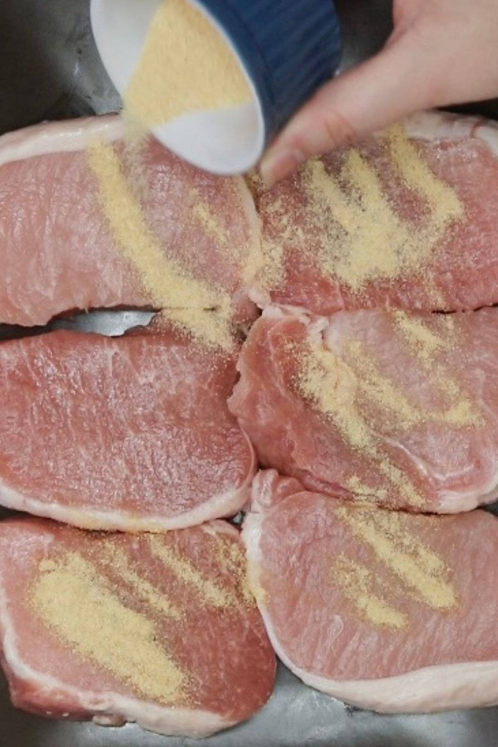 Sprinkling garlic powder onto pork chops.