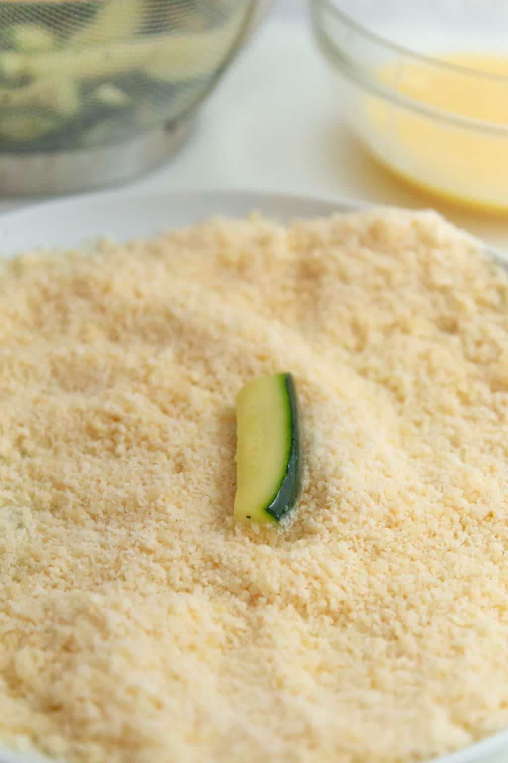 Zucchini being rolled in parmesan cheese.